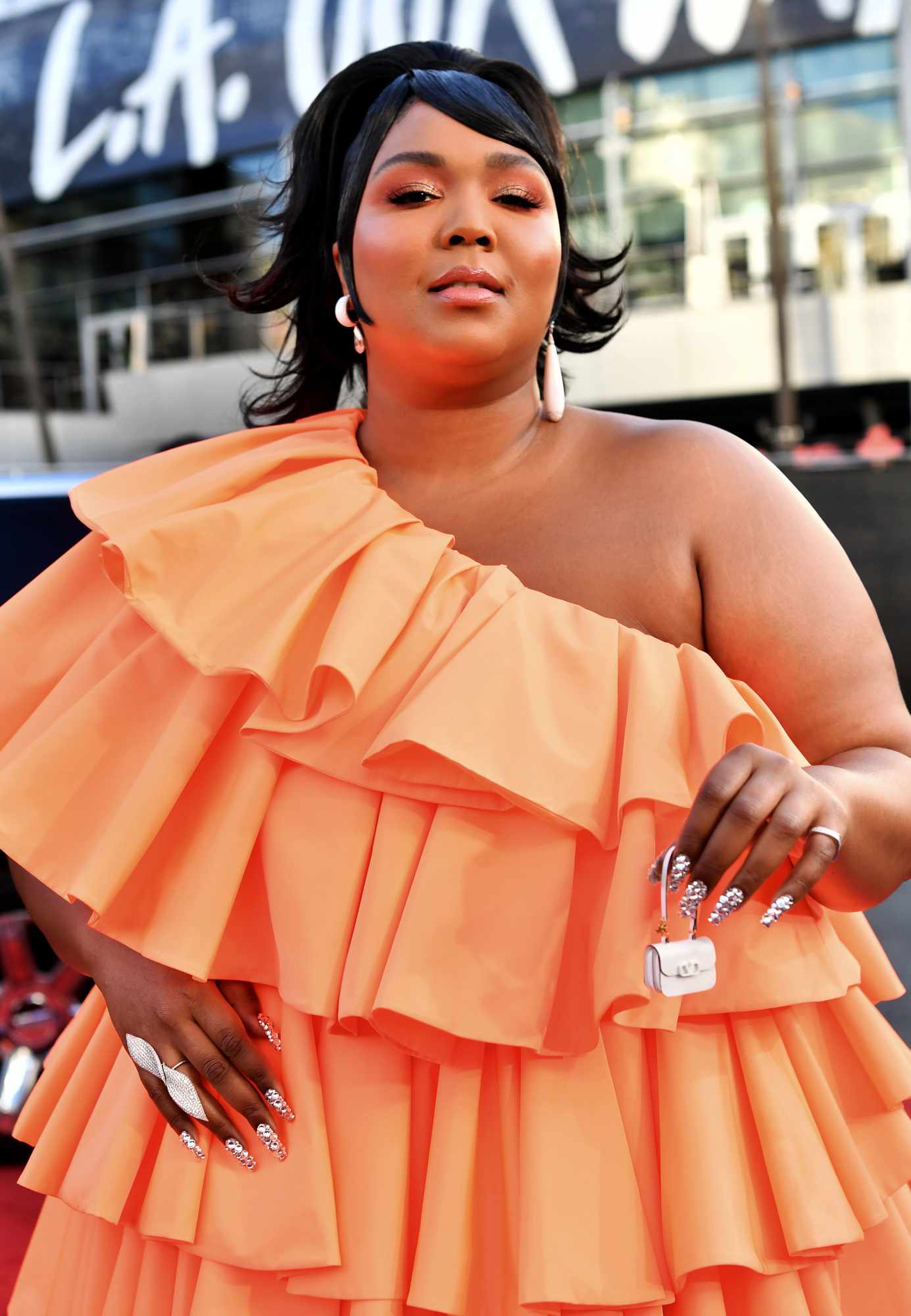 Lizzo wearing an orange one-shoulder ruffle dress