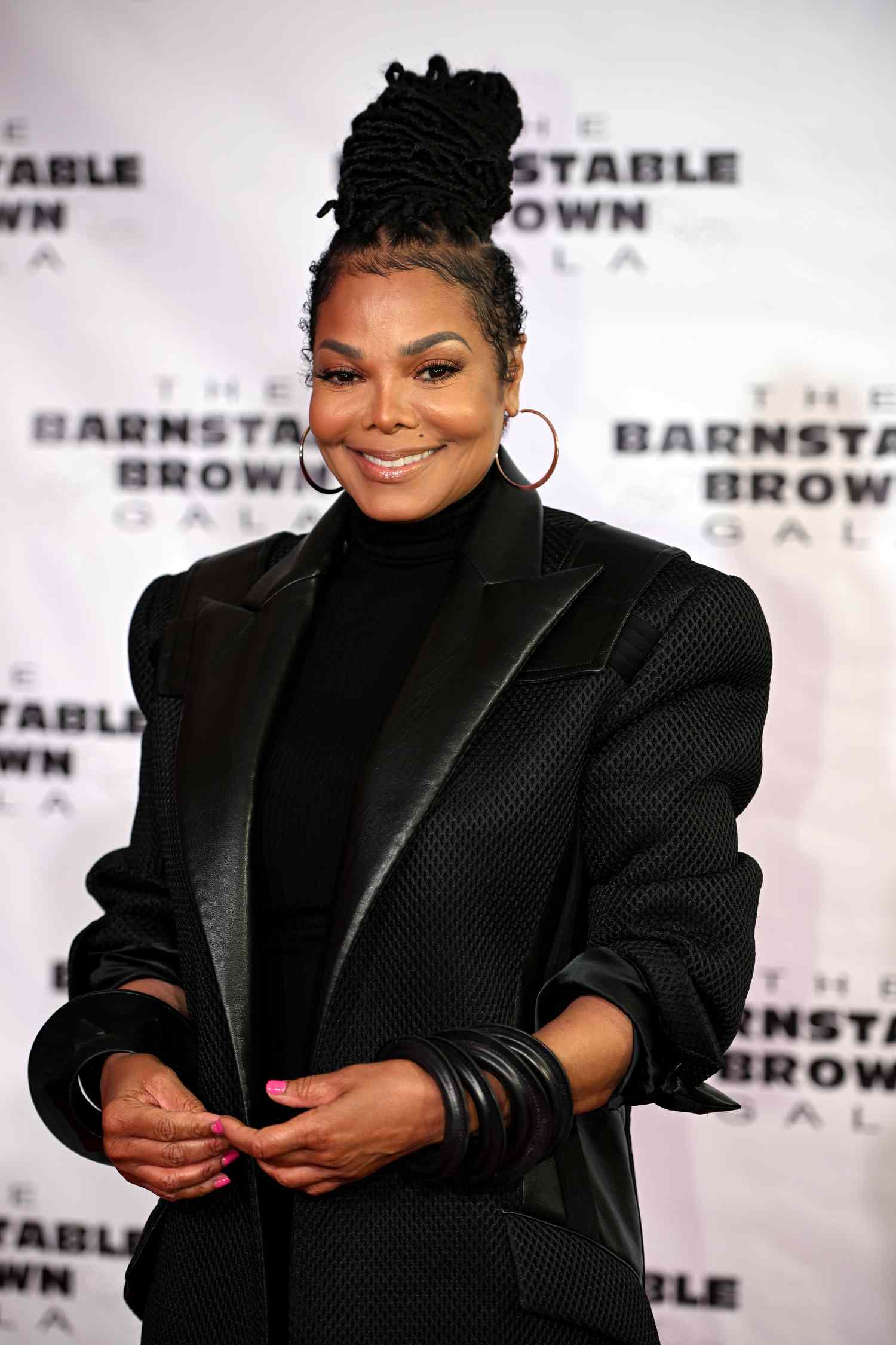 Janet Jackson with her hair in an updo and wearing a black blazer and turtleneck