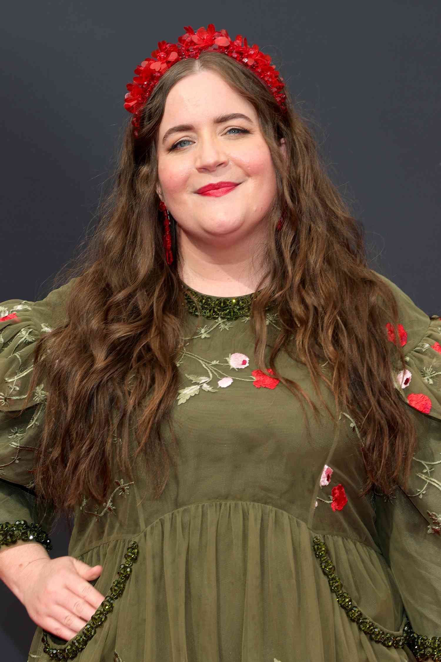 Aidy Bryant in an olive green dress with floral design and red headband