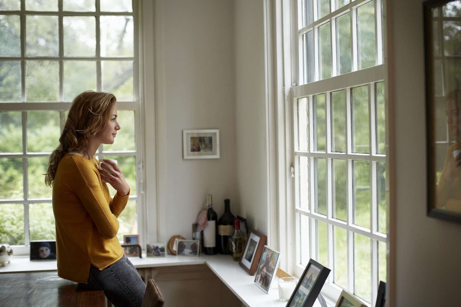 Side view of thoughtful woman looking through window while having coffee in cottage