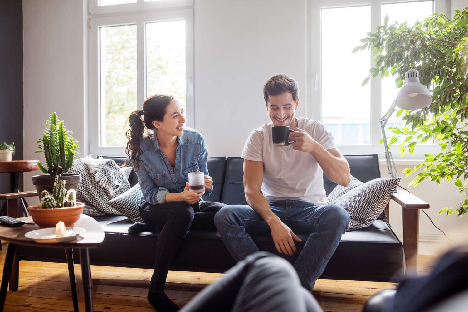 A woman and a man drinking coffee on a sofa and smiling 