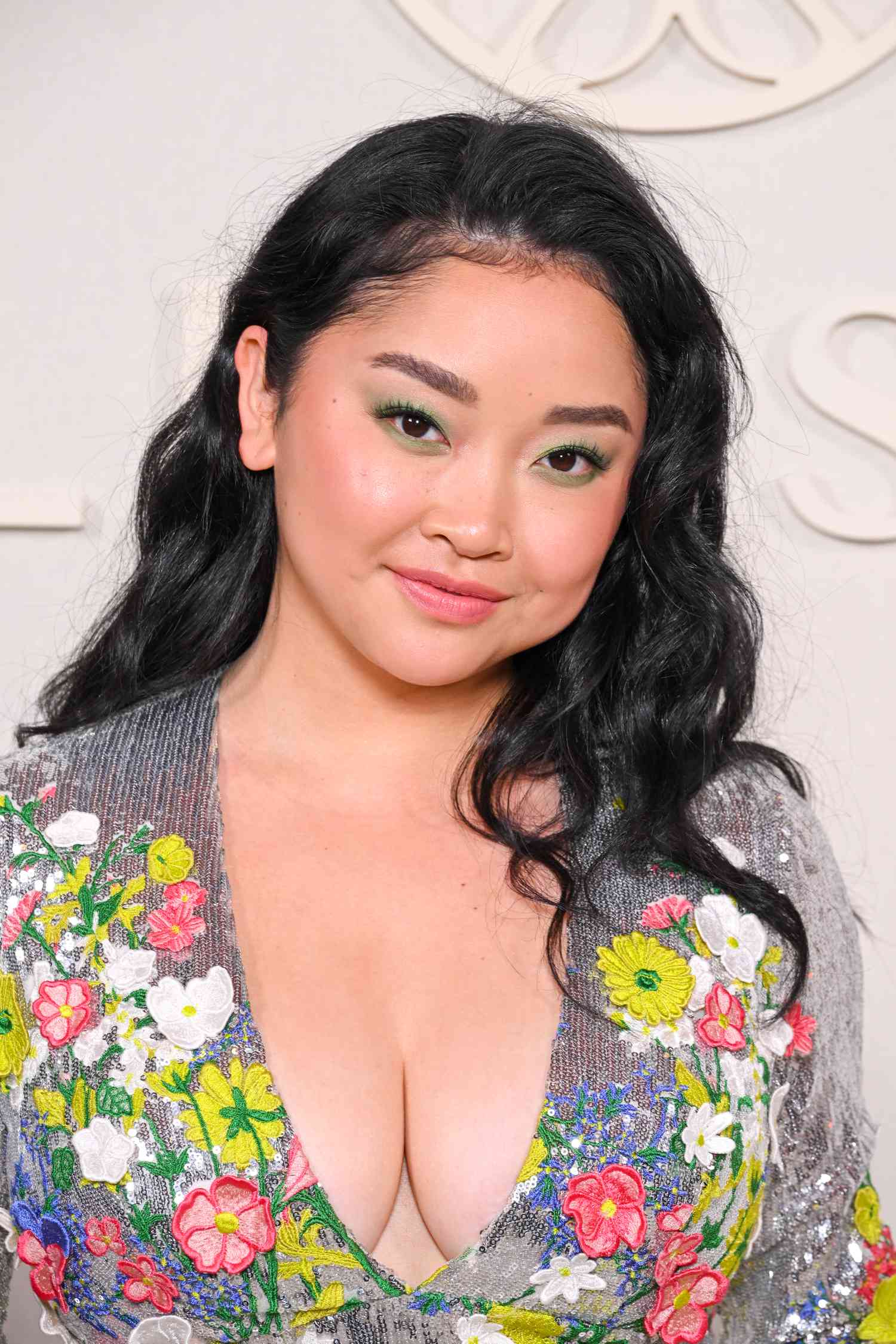 Lana Condor with long, wavy hair and a silver sequined dress with floral embellishments 