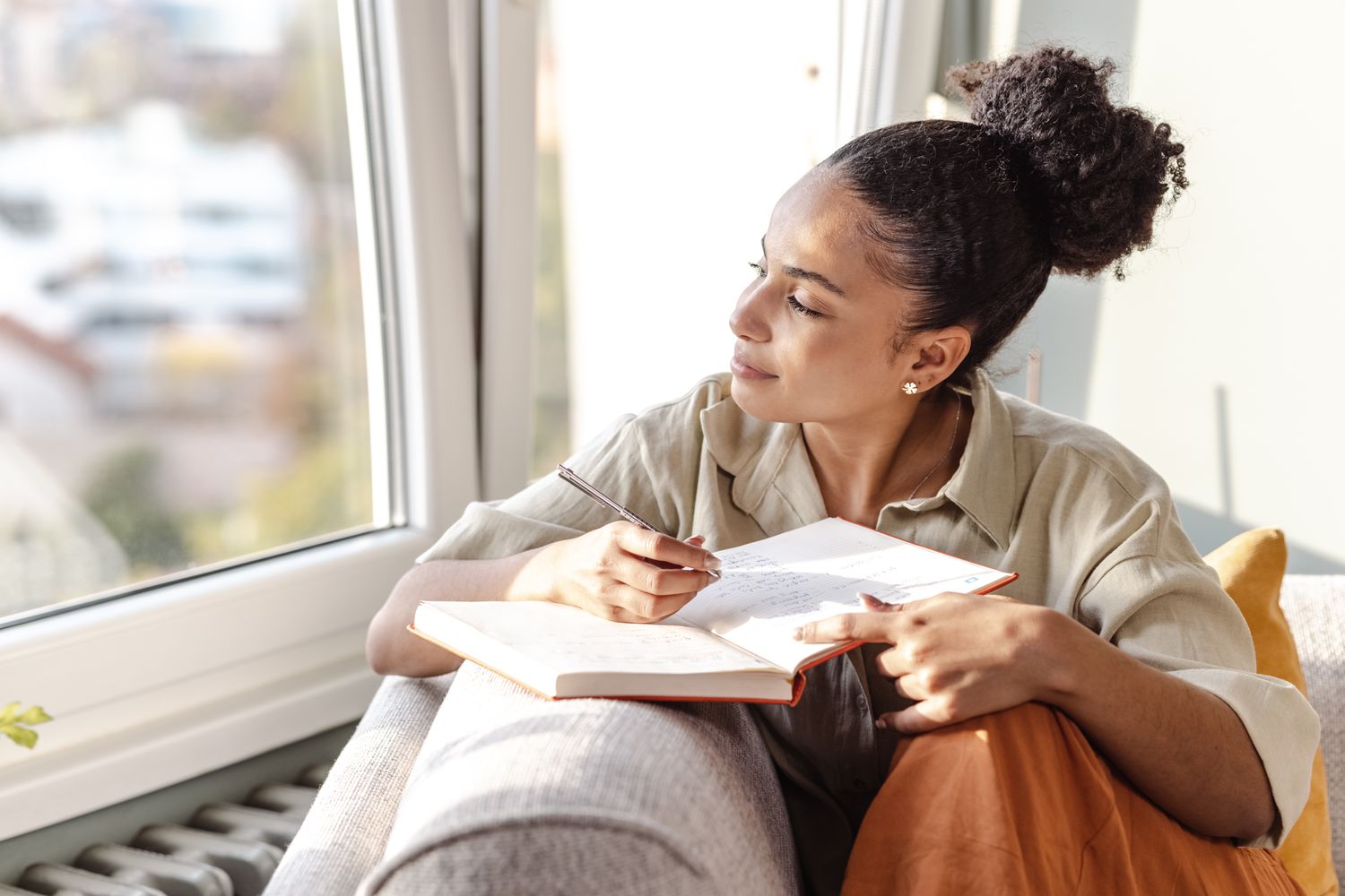 Woman sitting on couch with a journal and pen looking out the window