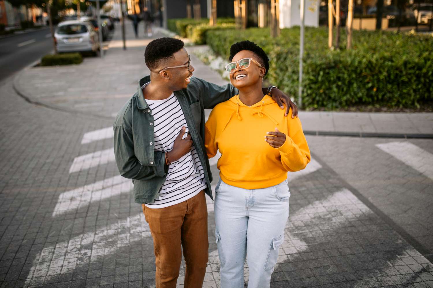 Two people laugh and embrace while walking across the street