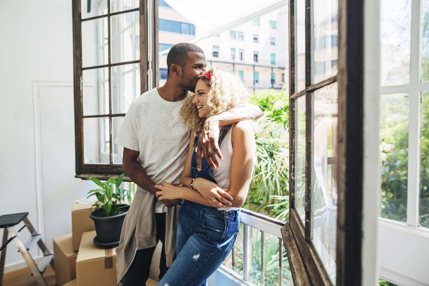 A couple stands smiling in front of a window with their arms around each other