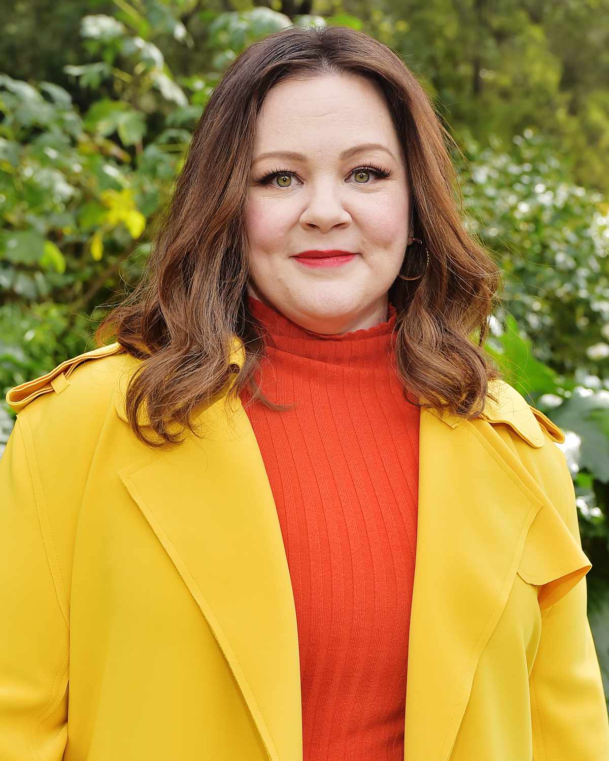 Melissa McCarthy wearing a yellow jacket over an orange turtleneck