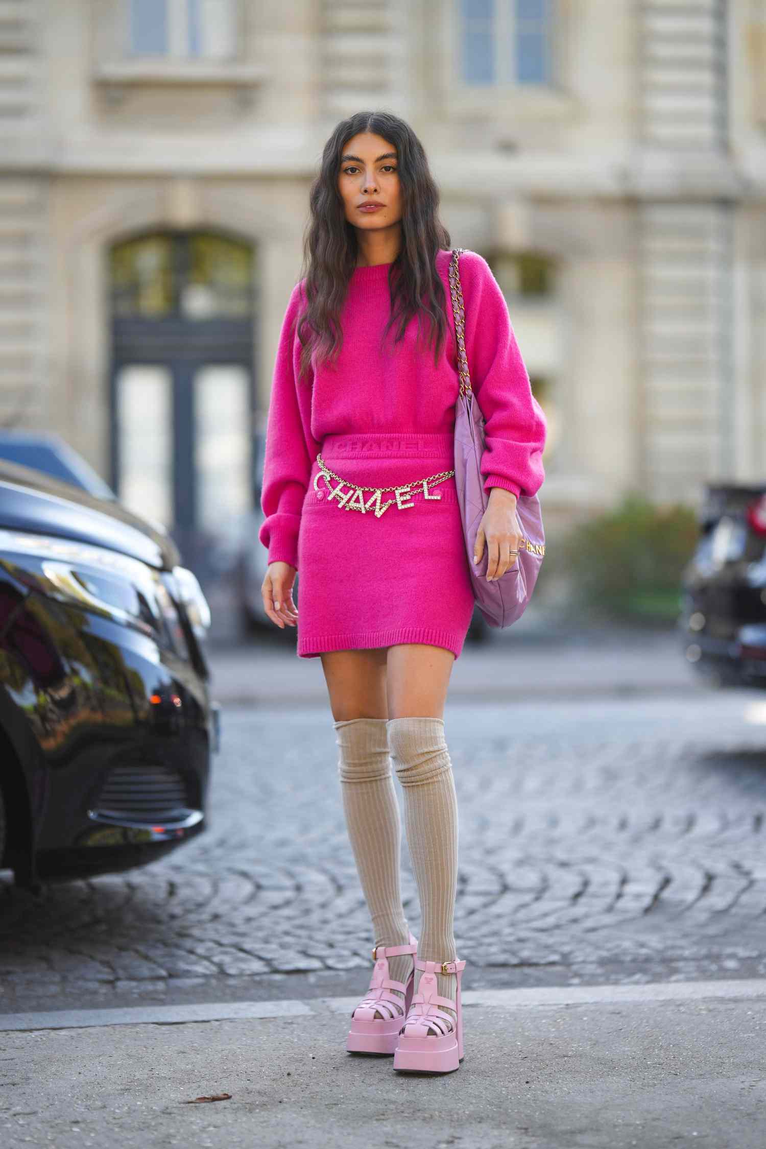 Person wearing a bright pink sweater dress with Chanel belt and platforms