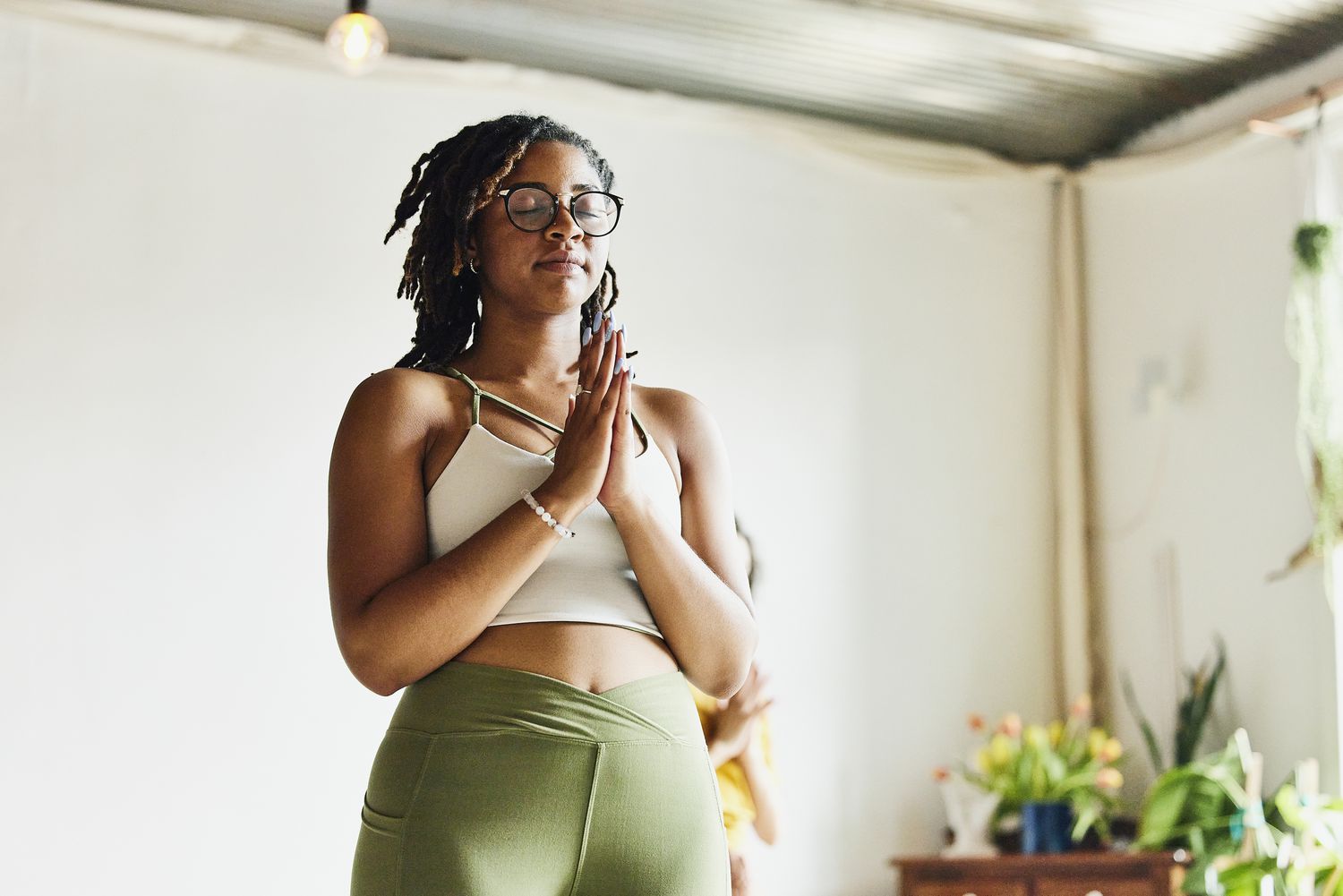 A woman wearing a white tank top and green yoga pants