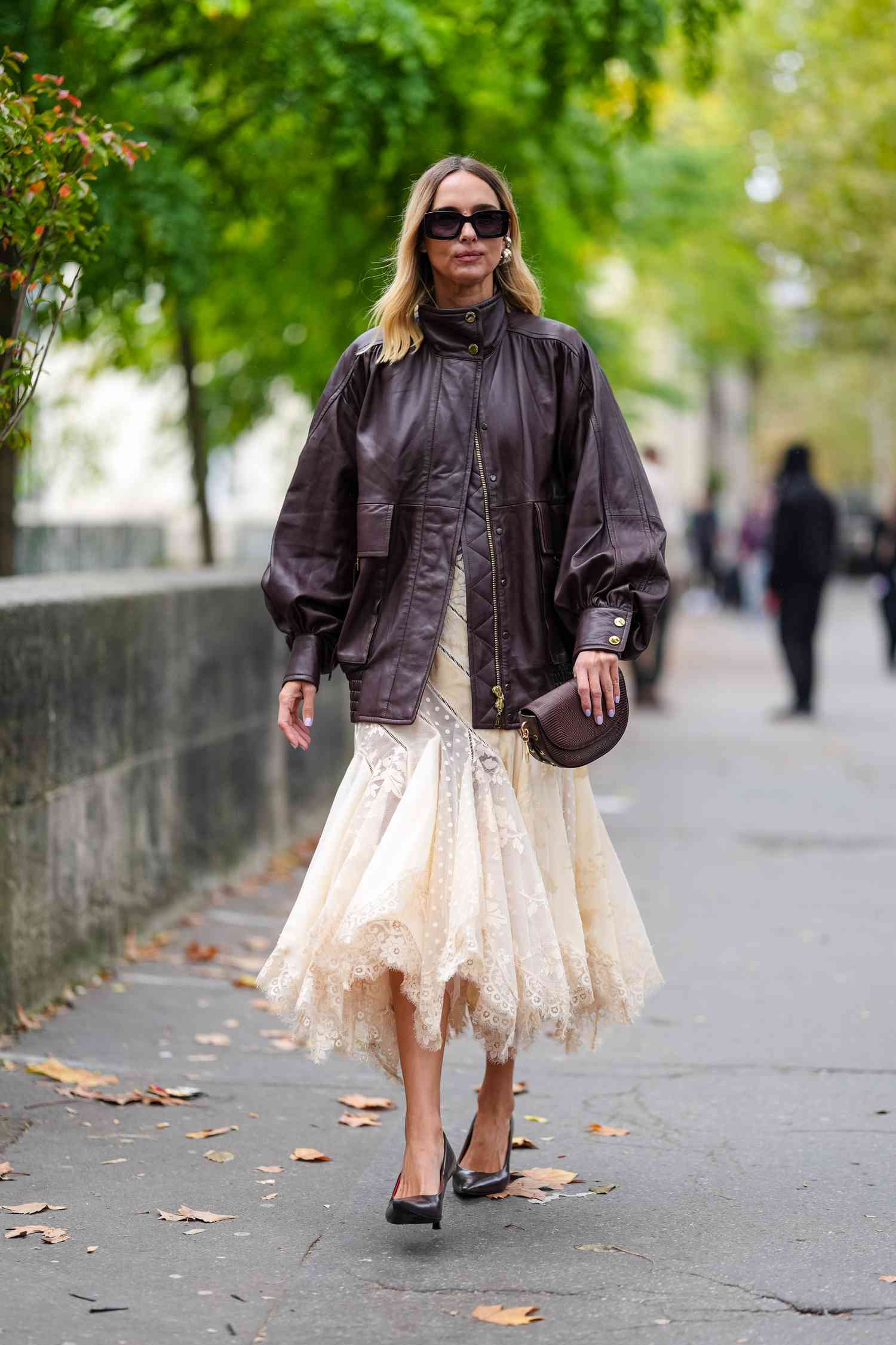 A woman wearing a chocolate brown leather jacket over a beige dress