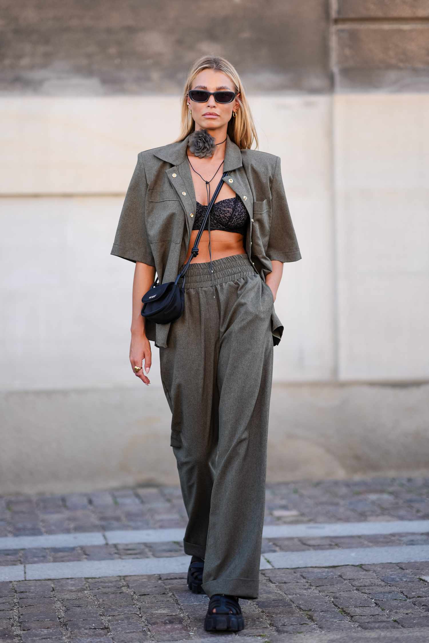 A guest wears black sunglasses, dark gray floral choker necklace, dark green oversized blazer short sleeve shirt, black lace bralette