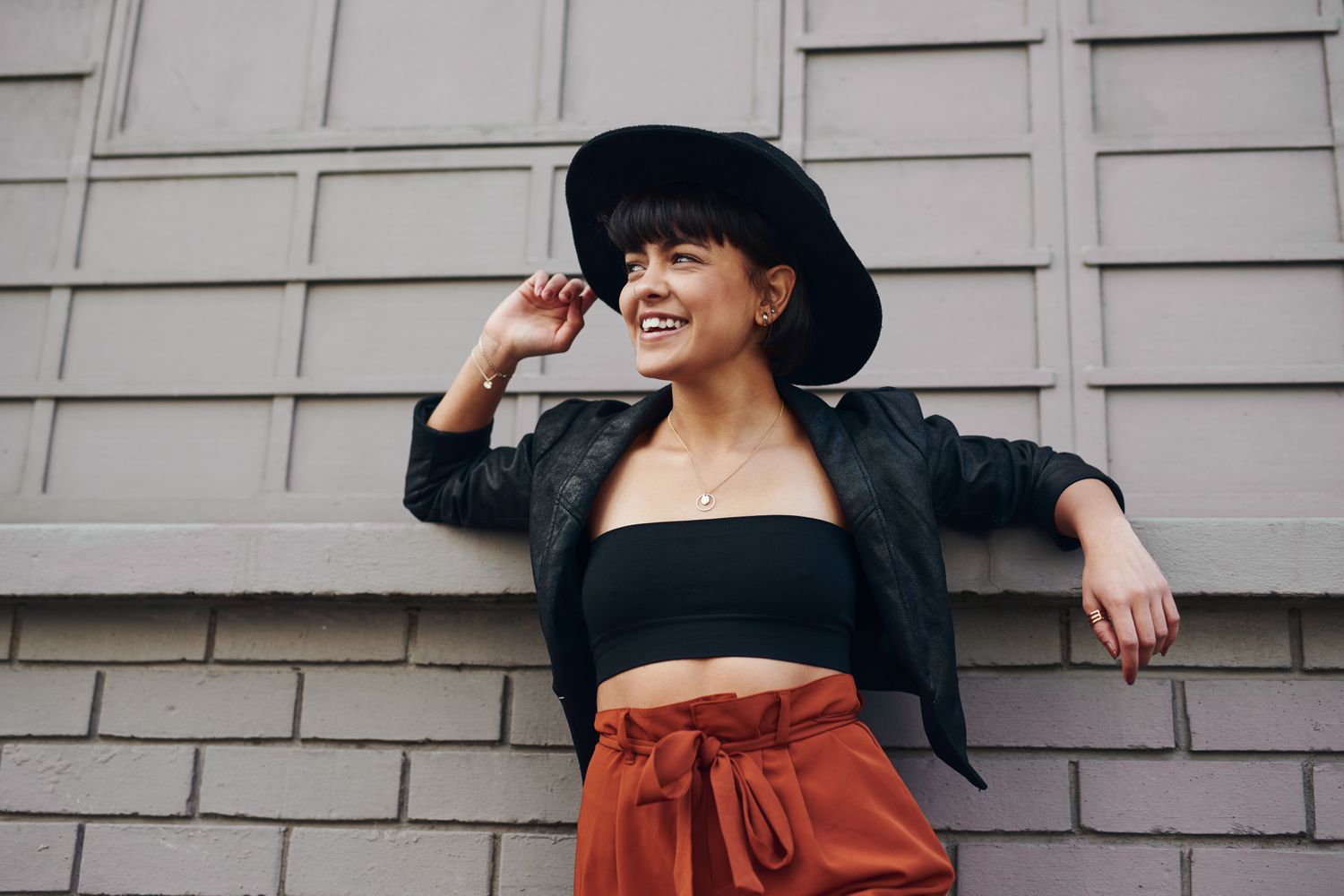 A woman wearing a black hat, black bandeau, black blazer, and orange pants