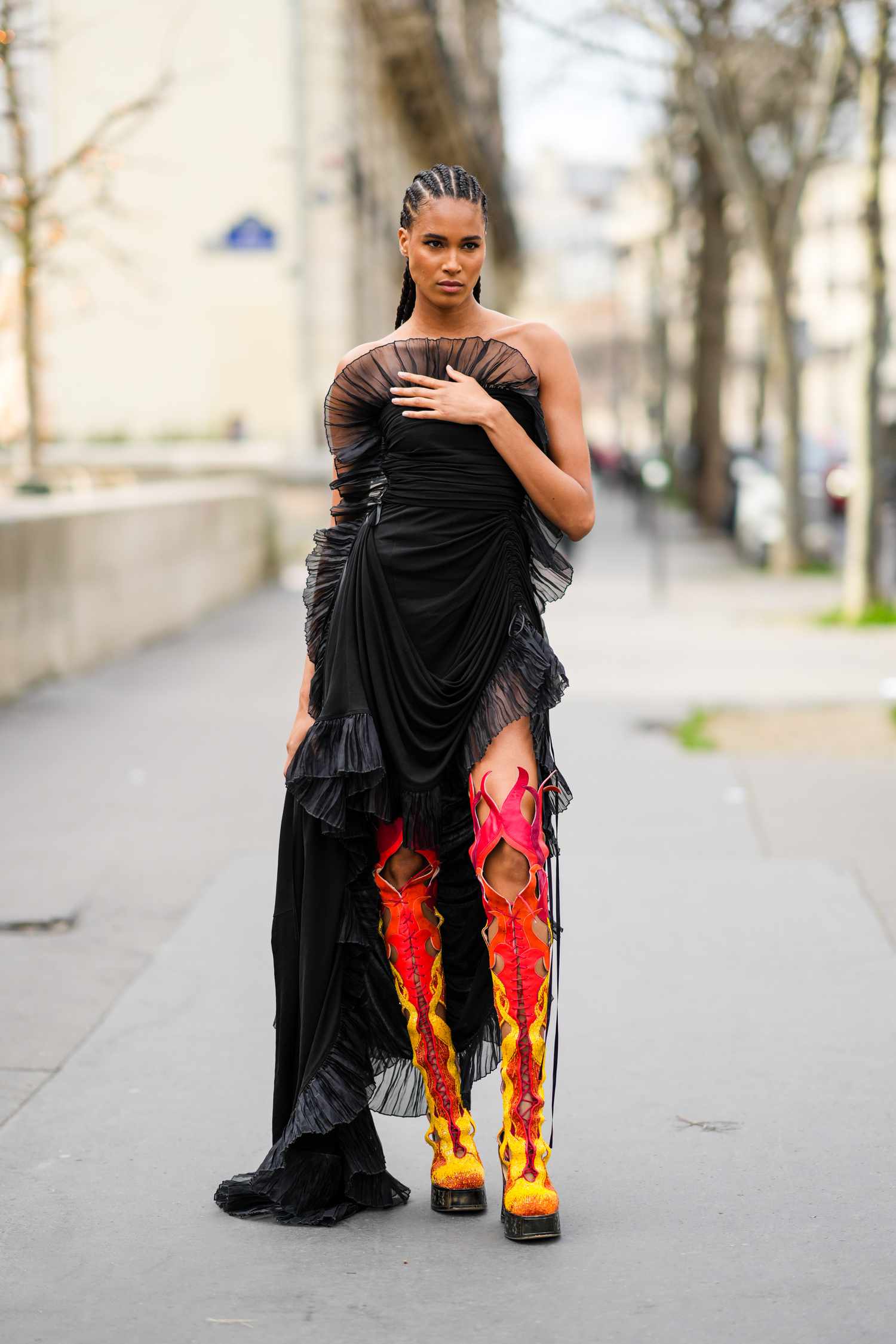 Cindy Bruna wears a black dress with ruffles and thigh-high boots with fire design