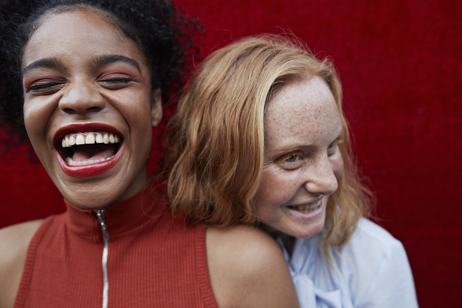 A woman laughs and another woman rests her face on her shoulder