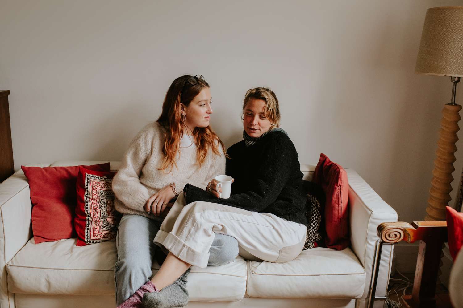 Two people sitting on a couch, one holding a cup, appearing engaged in conversation