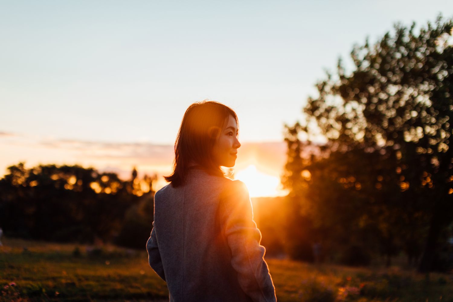 Person standing outdoors at sunset, backlit by the sun