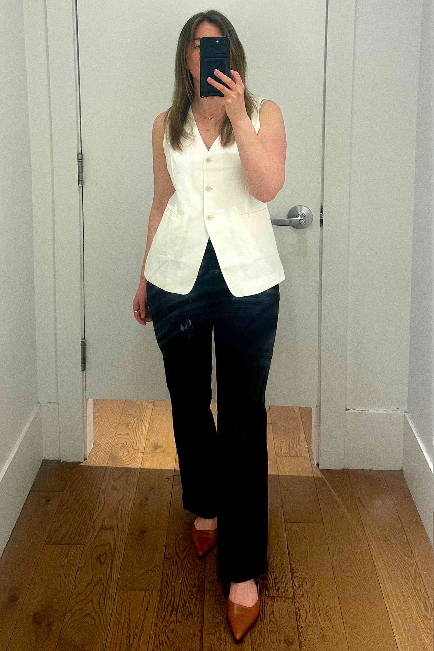 An individual standing in a room wearing a sleeveless vest and pants, taking a photo in a mirror