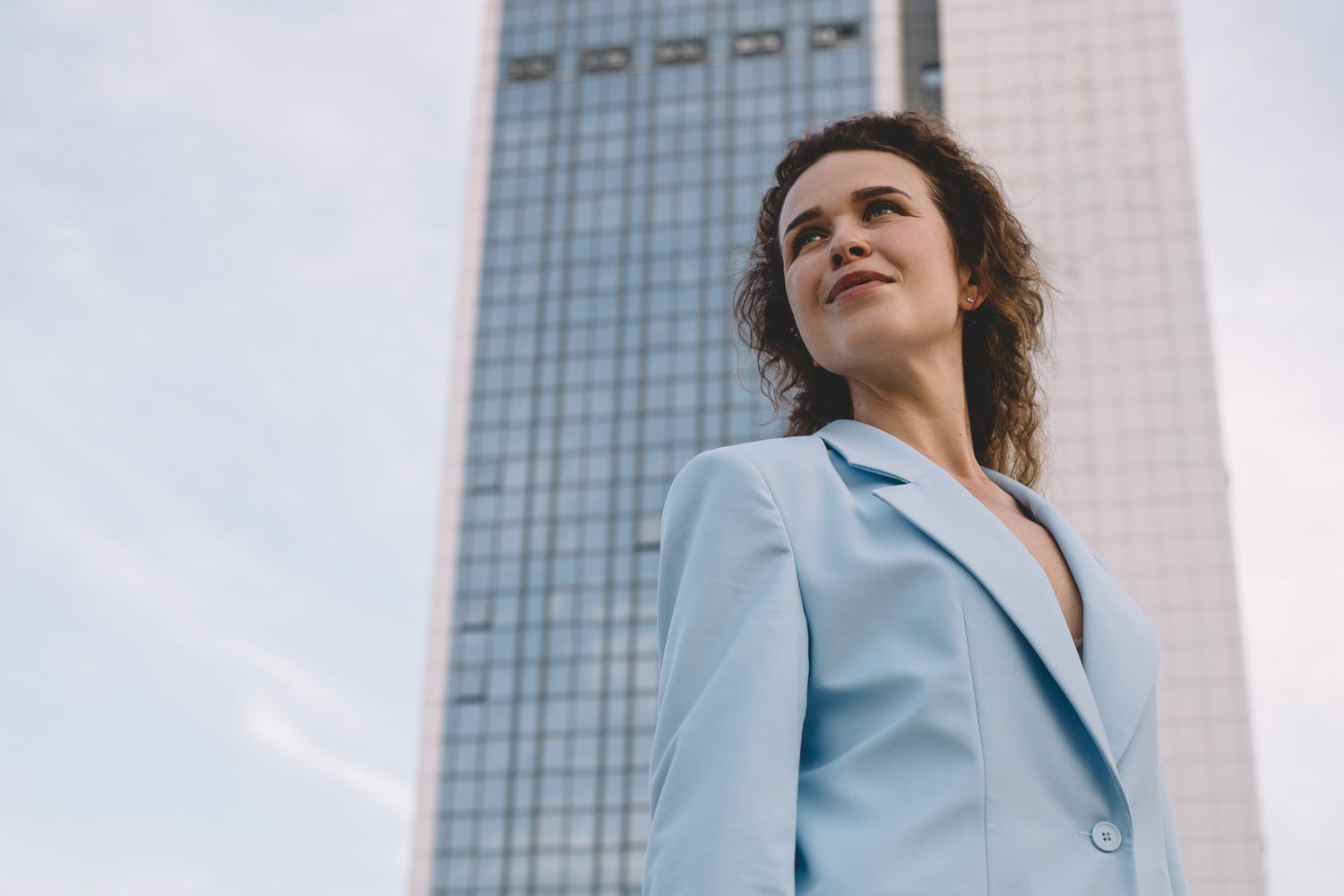Person standing outdoors in front of a tall modern building, looking upward