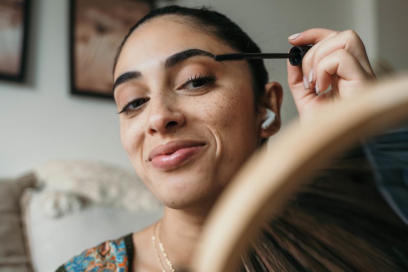 A person applying mascara while using a mirror