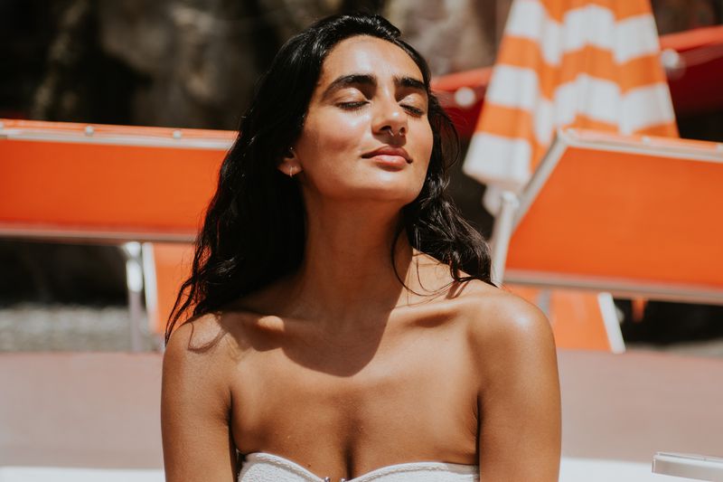 A woman relaxing by a pool with striped umbrellas in the background