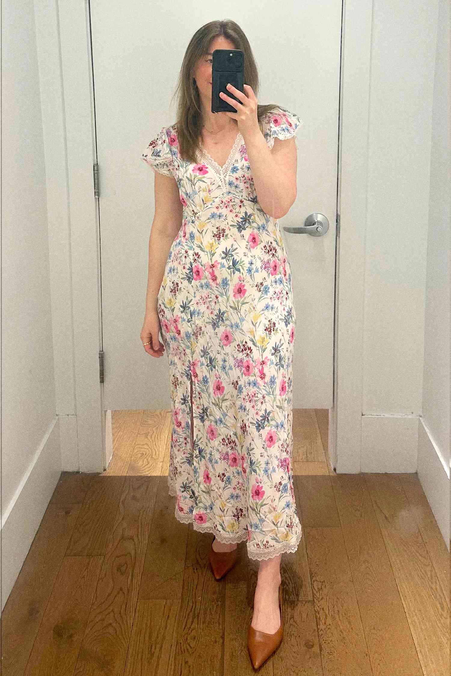 Person in a floral dress takes a selfie in a fitting room with a phone