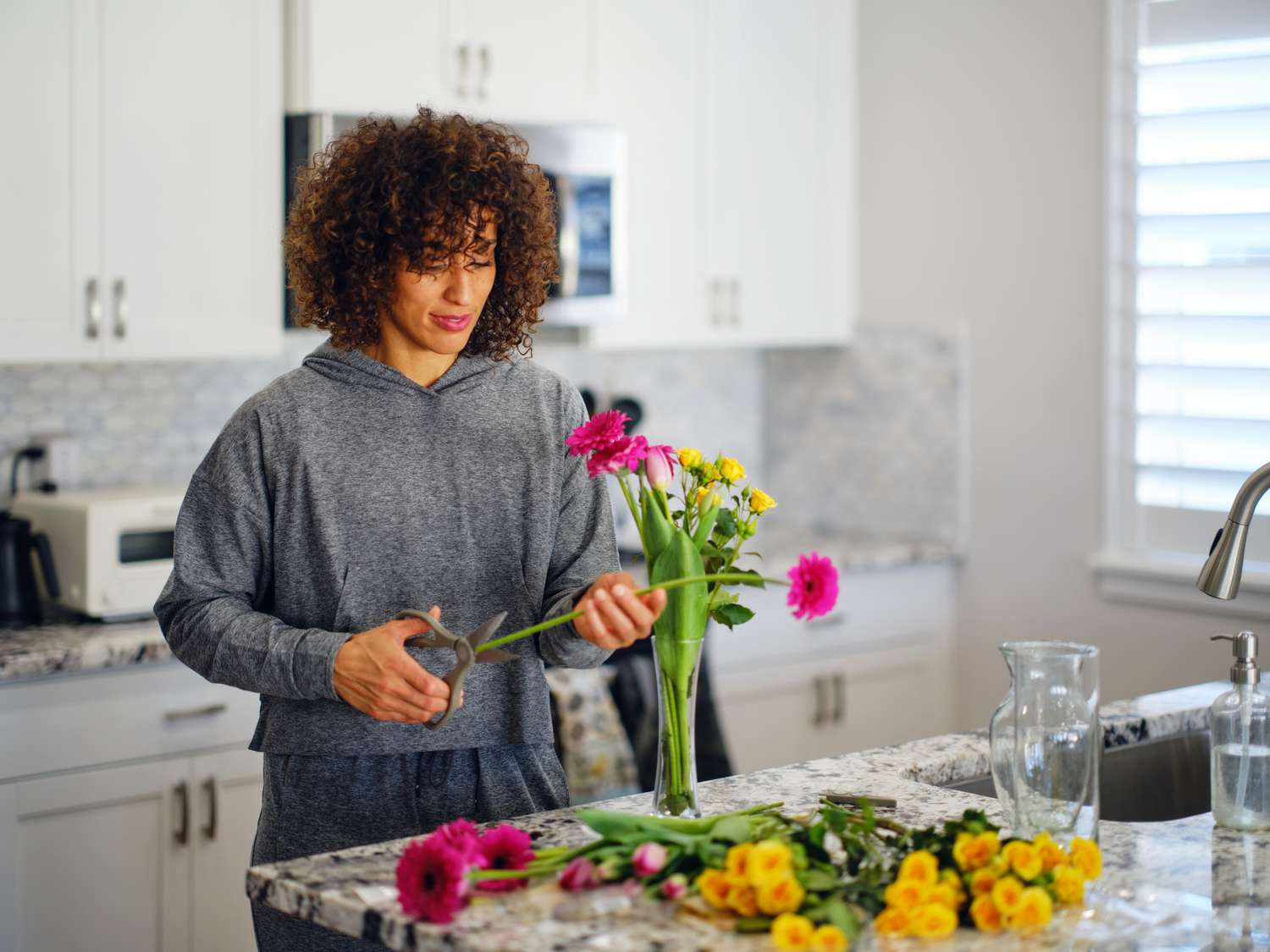 A woman in her home kitchen arranging fresh cut flowers into vases.