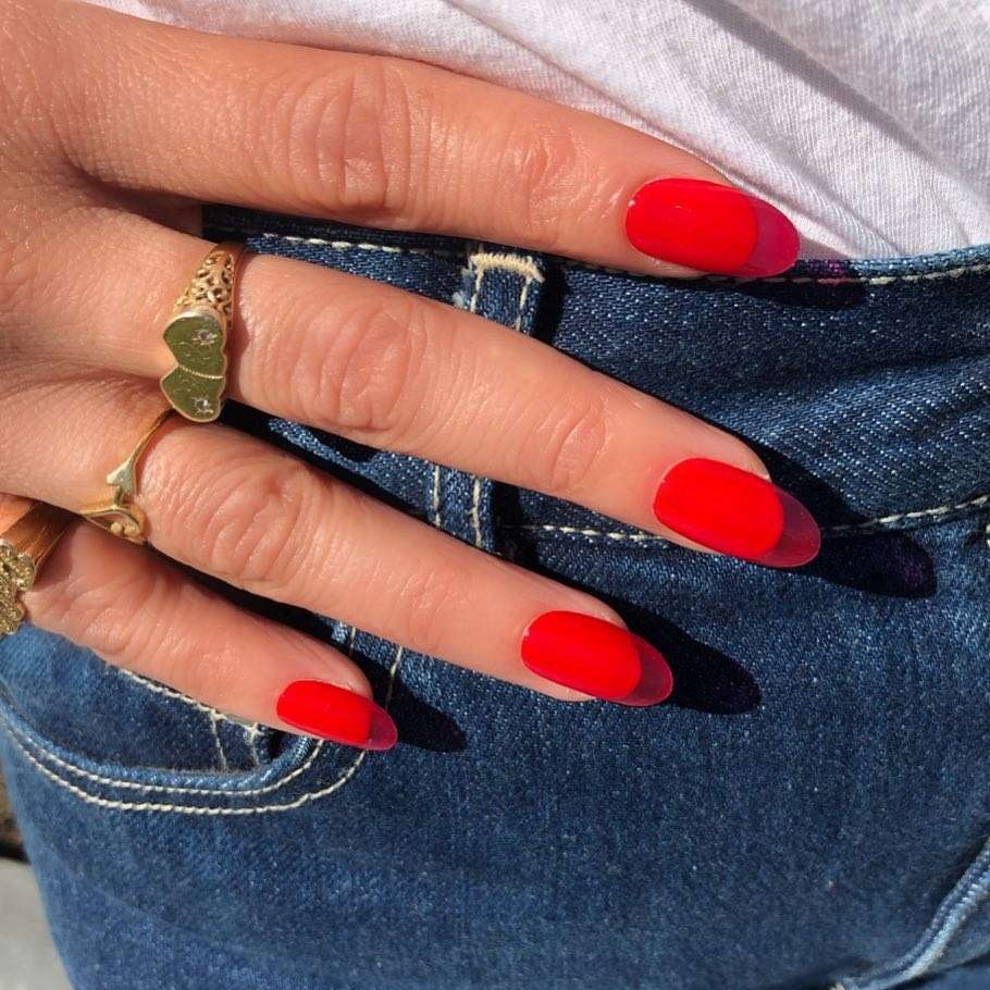 A person's hand with red painted nails and rings resting on the pocket of a pair of jeans