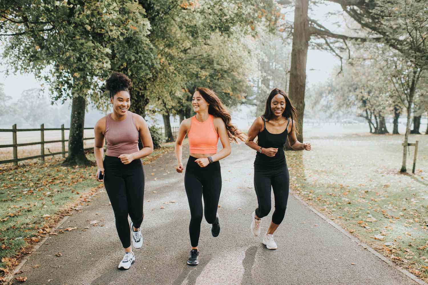 Three women jogging on a park path surrounded by trees