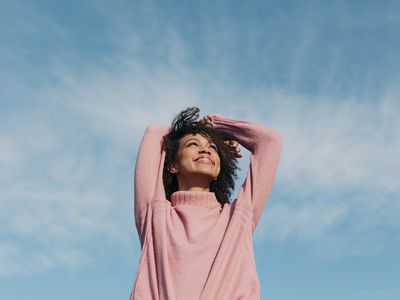 Person in a pink turtleneck sweater looks up at the bright blue sky