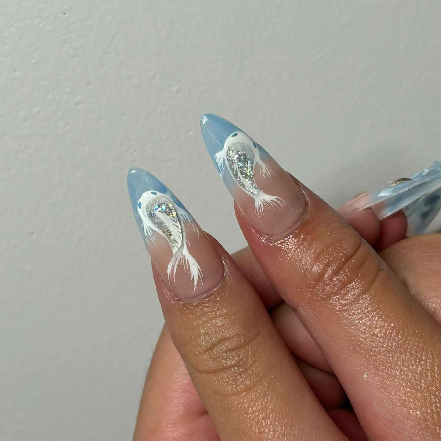 Close-up of hands with detailed nail art featuring painted fish designs