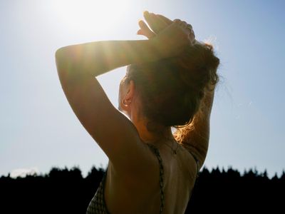 Person standing outdoors with arms raised, sunlight shining above
