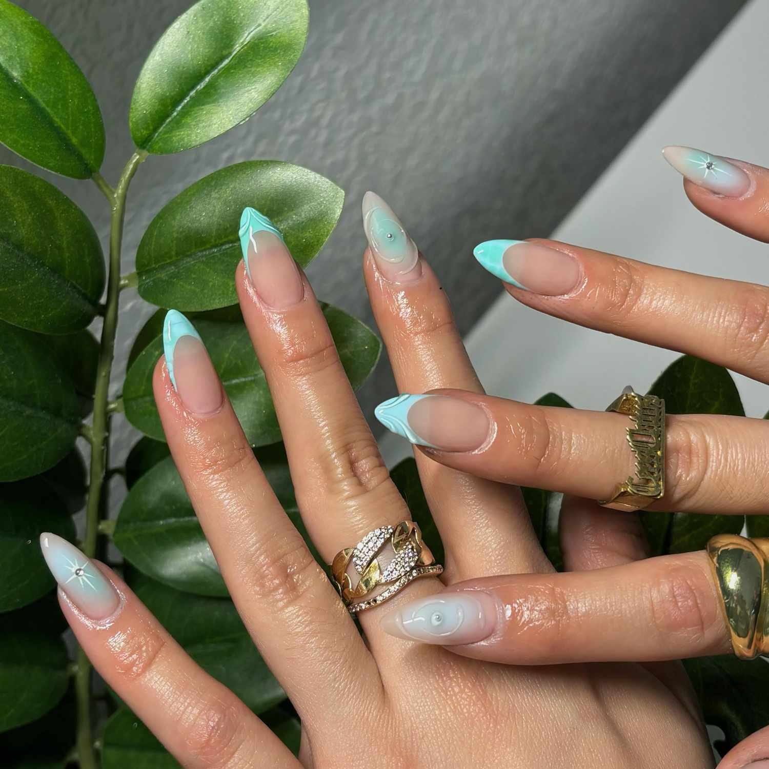 Hands with manicured blue nails featuring a light design and worn gold rings