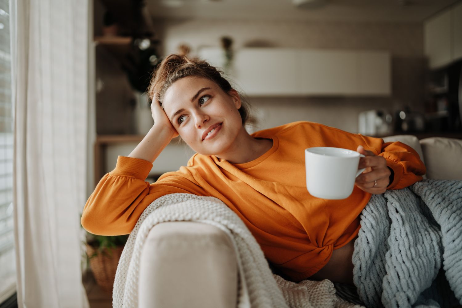 Person relaxing on a couch holding a mug, looking thoughtful