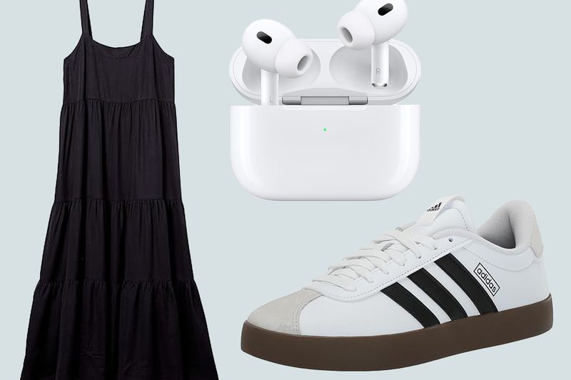 A black sleeveless tiered dress, white wireless earbuds in their case, and a white sneaker with black stripes