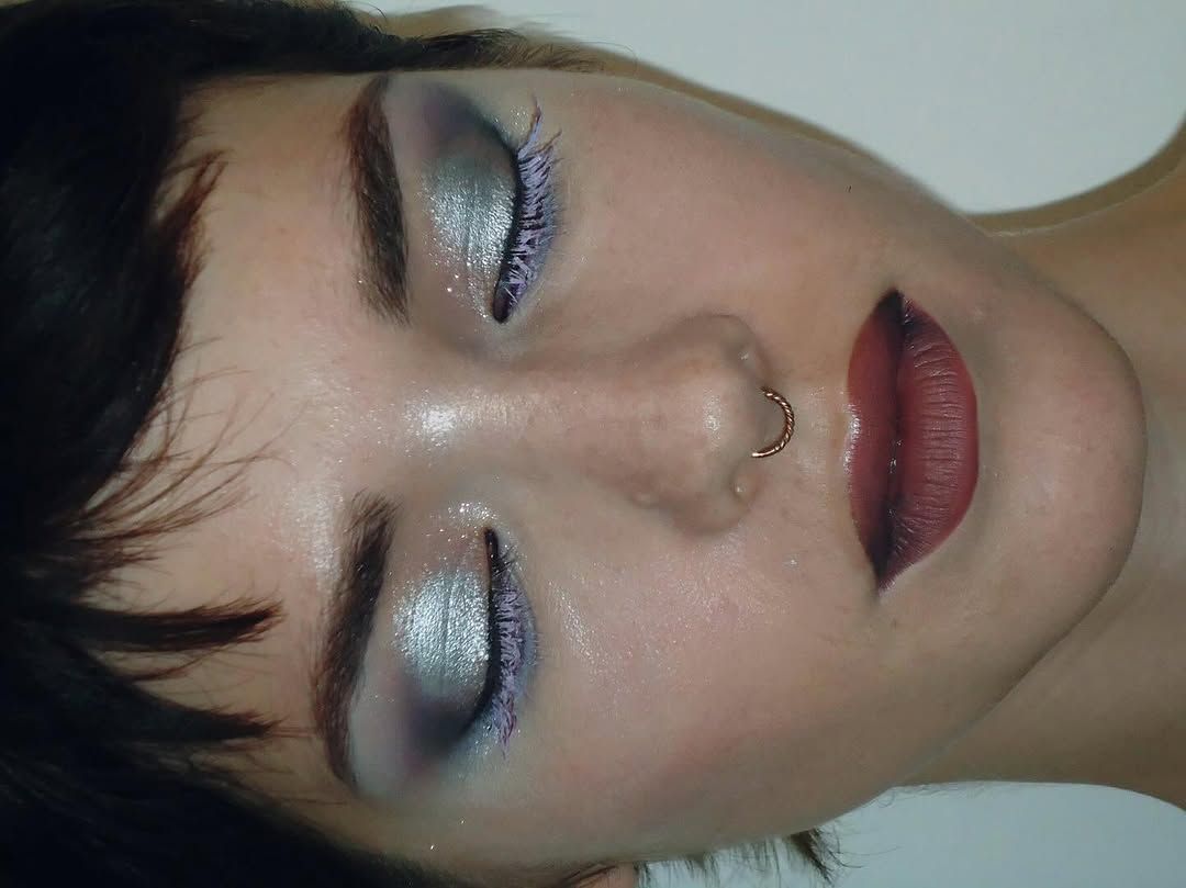 Close up of a person on their side with their eyes closed showing silver and purple eyeshadow