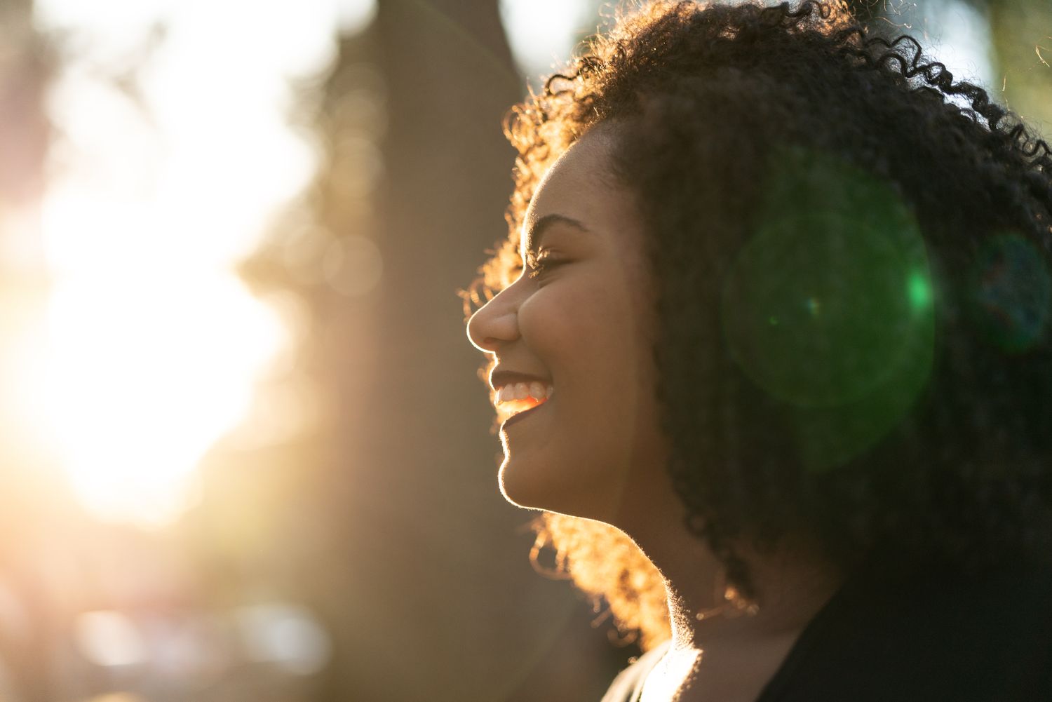 A person smiling in profile view with sunlight in the background outdoor setting focus on expression