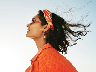 Side view of a person with short, dark hair and orange headband looking up at the day sky