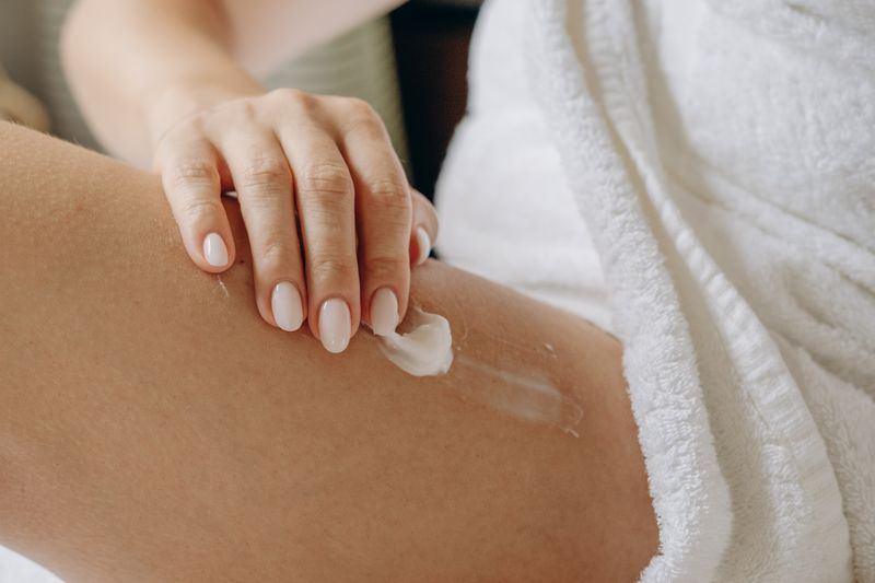 Person applying cream to their leg while wearing a towel