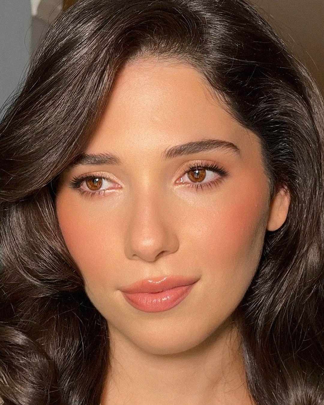 A close up of a person with wavy brown hair and light makeup