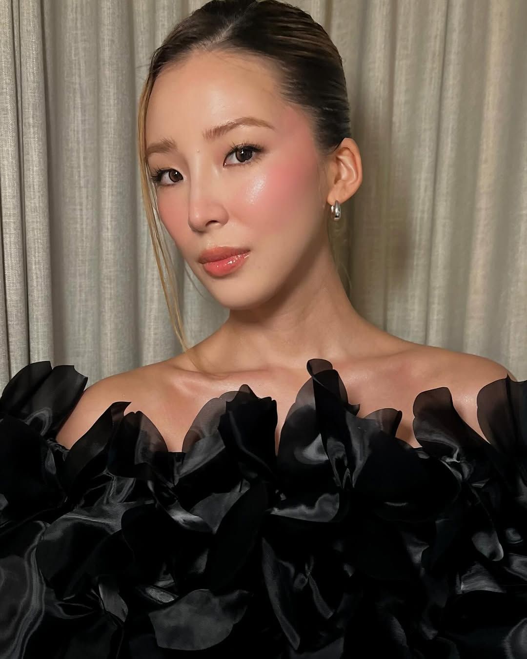 A person with rosy blush and a ruffly black garment