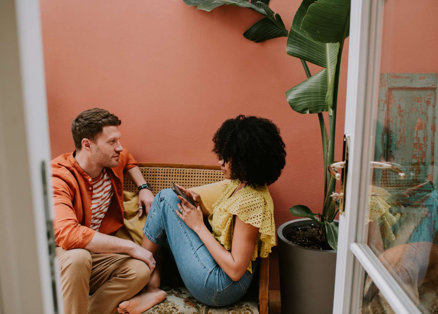 A couple sitting on a rattan seat against a pink wall