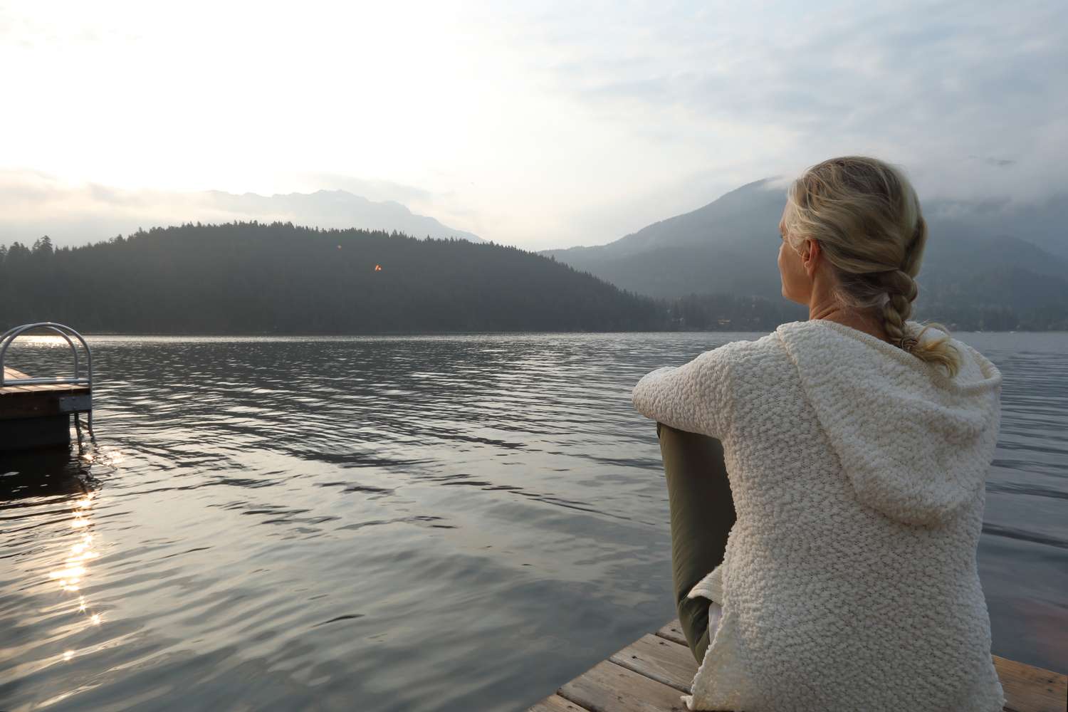 Woman sitting on a doc in a white sweatshirt and green leggings looking contemplative