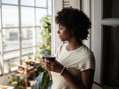 A person holding a cup and looking out of a window in a city setting