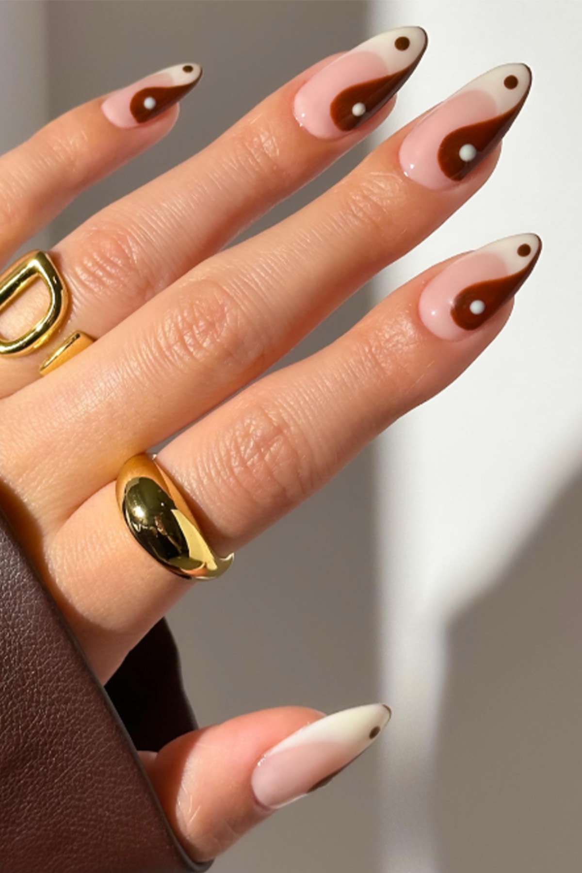 Hand with nail art featuring a yinyang pattern and wearing gold rings