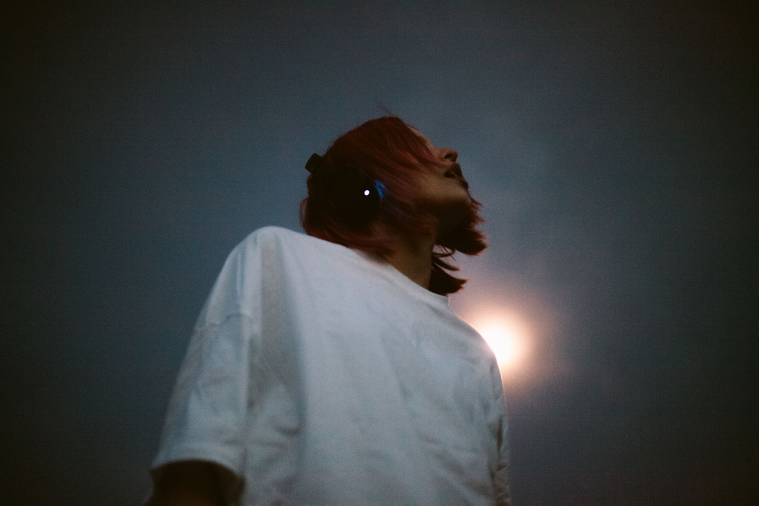 Young woman listening music in headphones standing against the sky at night