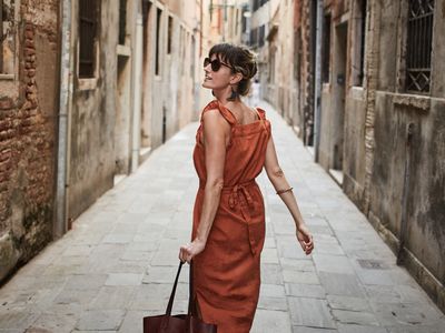 A woman walking down a narrow street carrying a bag looking up
