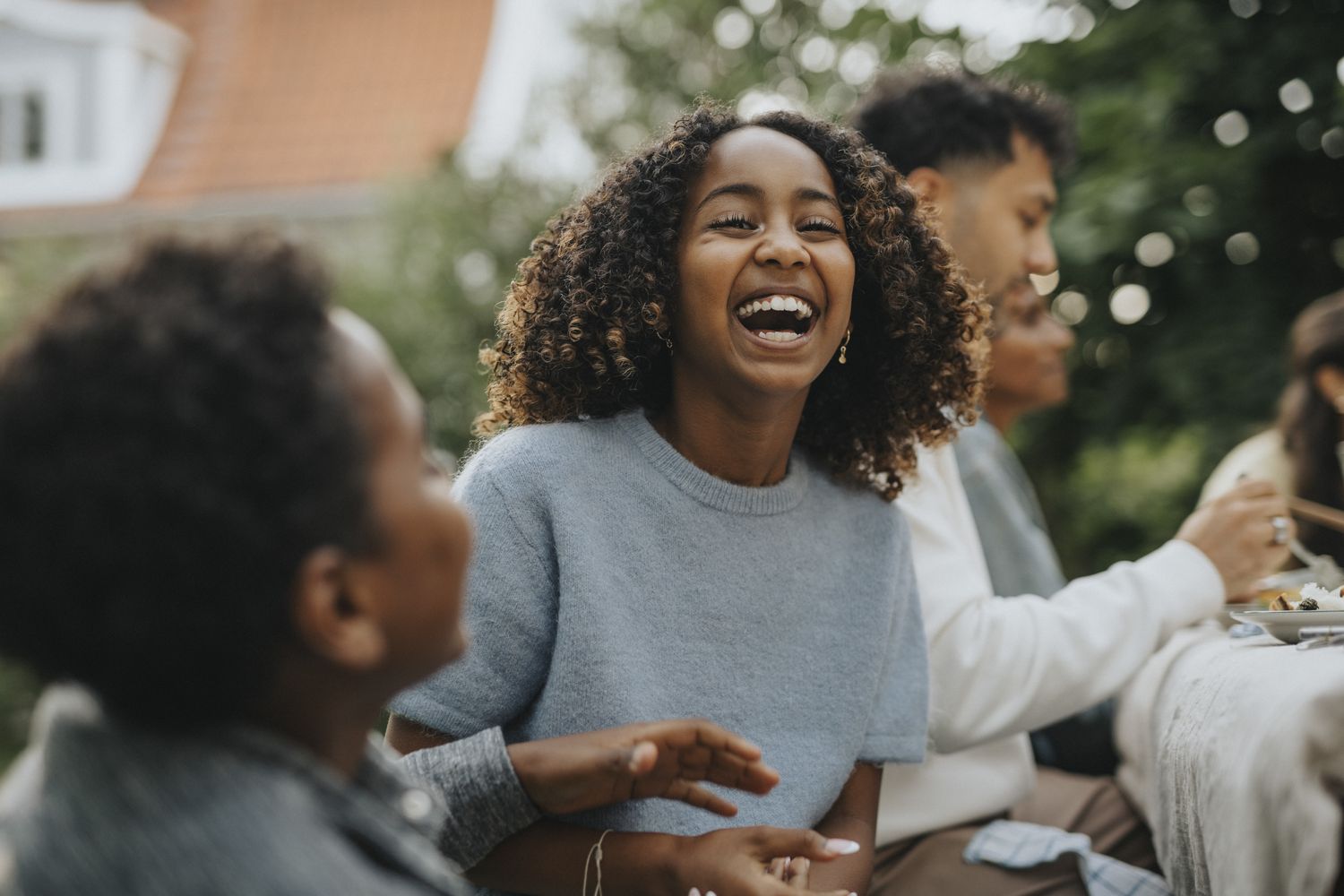 Woman in blue sweater laughing sitting next to her sibling