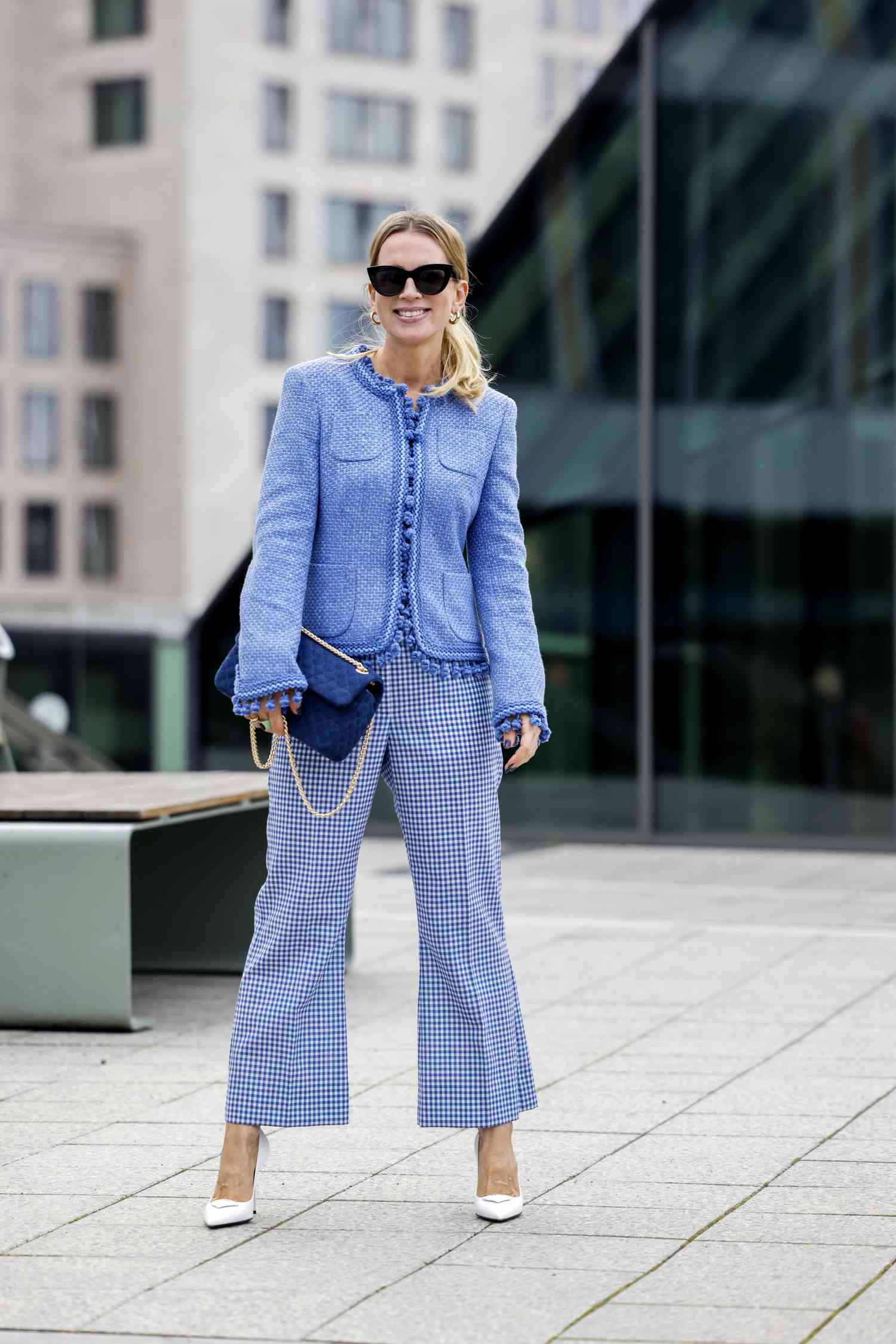 Blonde person wears black sunglasses, a blue jacket, blue-and-white checkered pants, and white heels
