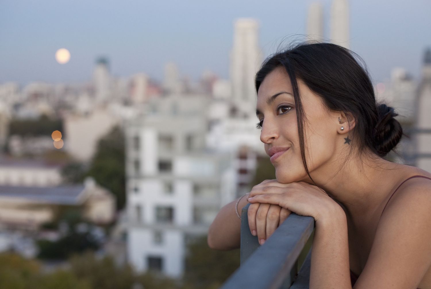 Woman on a balcony looking out at the horizon with a full moon in the background