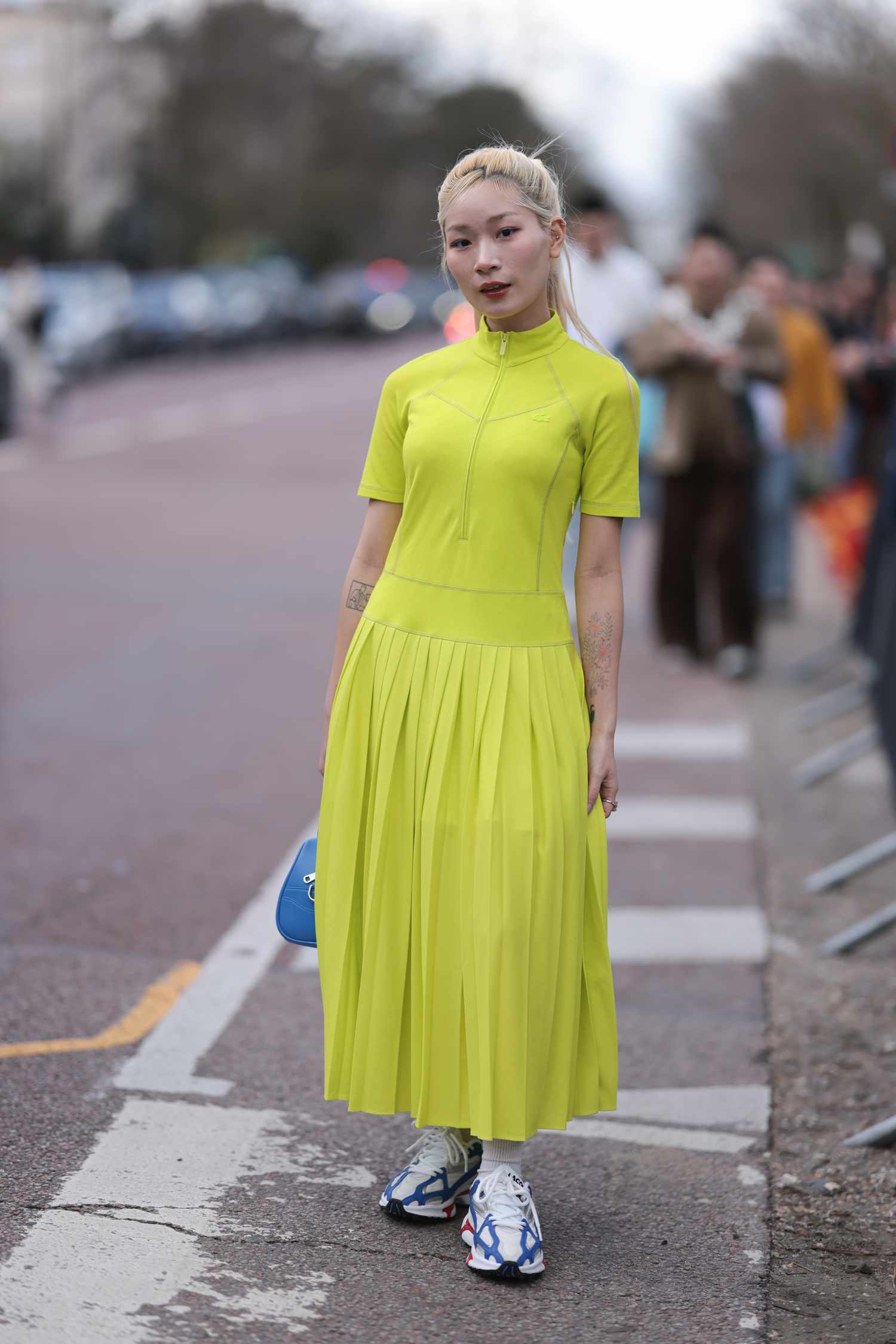 Blonde person with their hair up wears a short-sleeve neon lime dress and sneakers