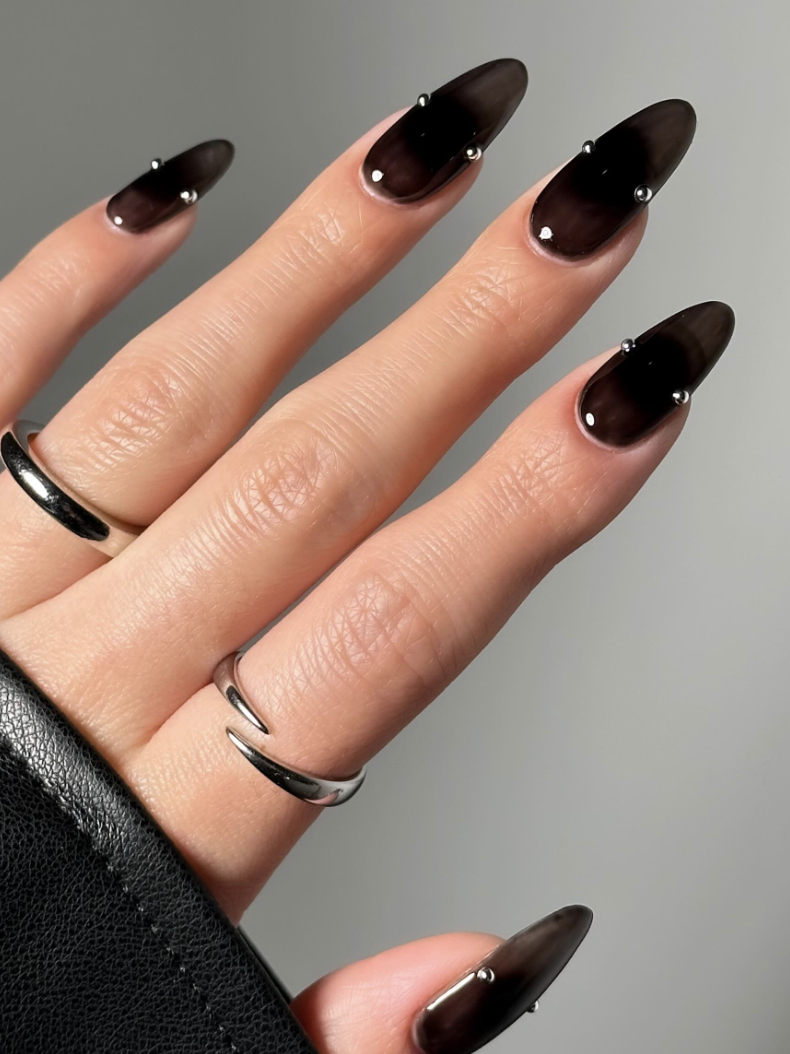 A hand with dark polished nails adorned with rings resting on a textured surface